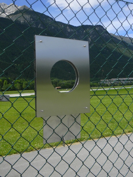 Spotterloch: Metallrahmen mit runder Öffnung im Flughafenzaun Innsbruck